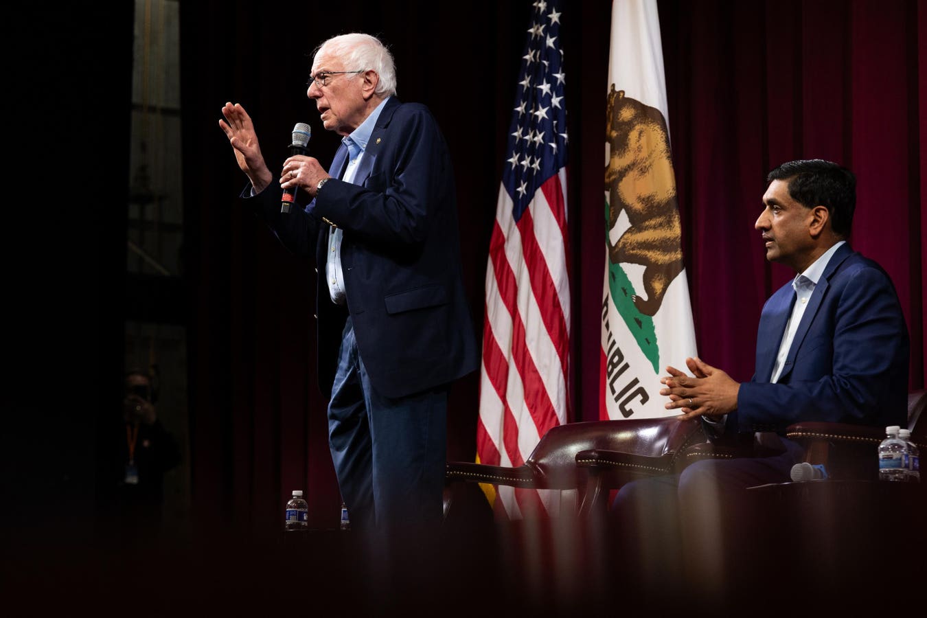 Senators Bernie Sanders and Ro Khanna speaking at a podium about their billionaire wealth tax bill